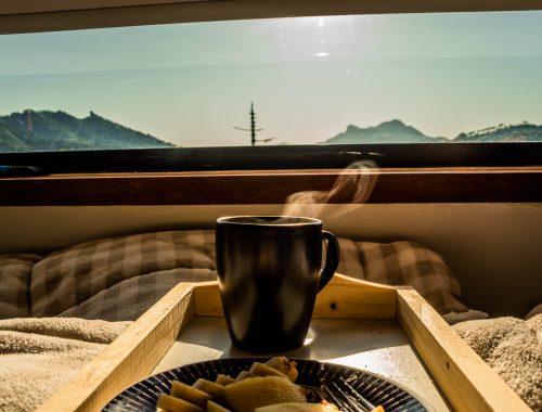 Xícara de café quente com vista da janela do quarto para as montanhas em um chalé-container para viagens por temporada